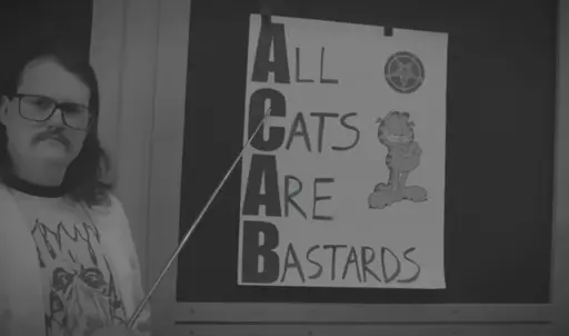 A man holding a stick pointing to a poster with the words 'All Cats Are Bastards' written next to a picture of Garfield.