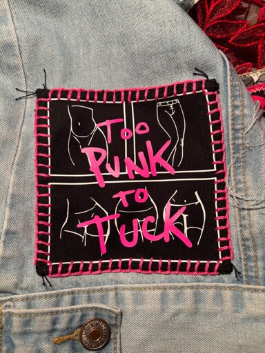 A patch sewn onto a denim jacket with bright pink thread that says “to punk to tuck” in a matching pink font